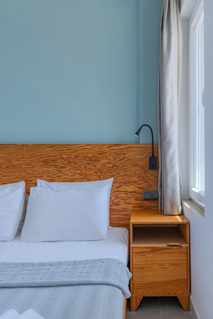 A minimalistic bedroom with wooden elements, white bedding, and light blue walls.